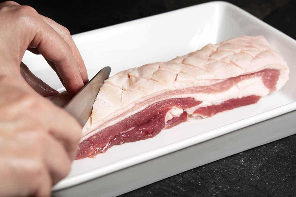 scoring pork belly skin in a diagonal pattern with a sharp knife