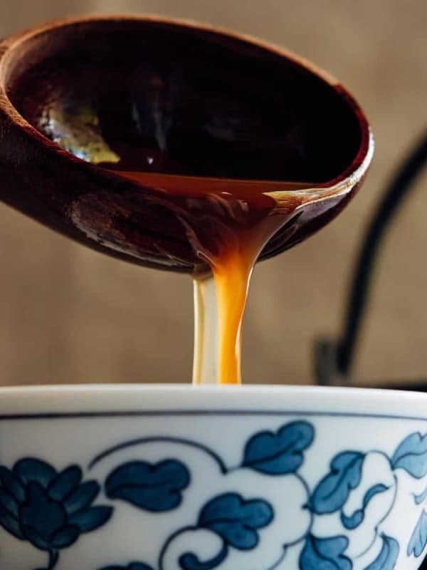 ladling shoyu ramen broth into a Japanese bowl.