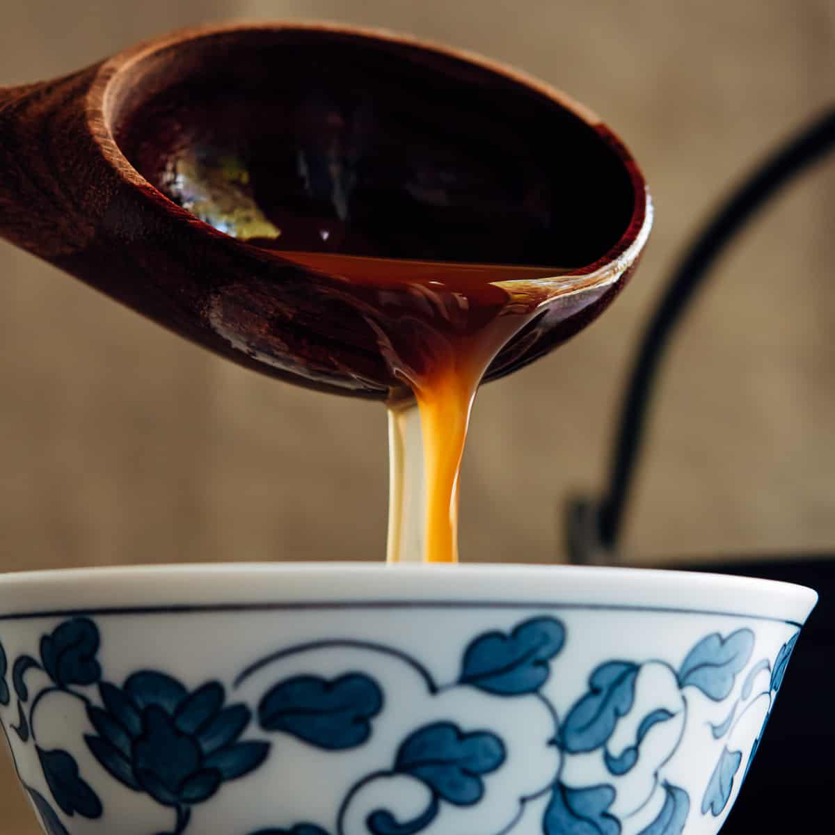 ladling shoyu ramen broth into a Japanese bowl.