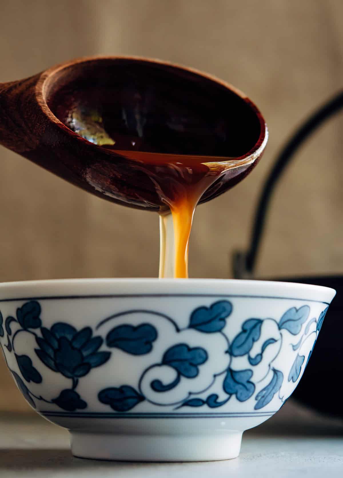 ladling shoyu ramen broth into a Japanese bowl.