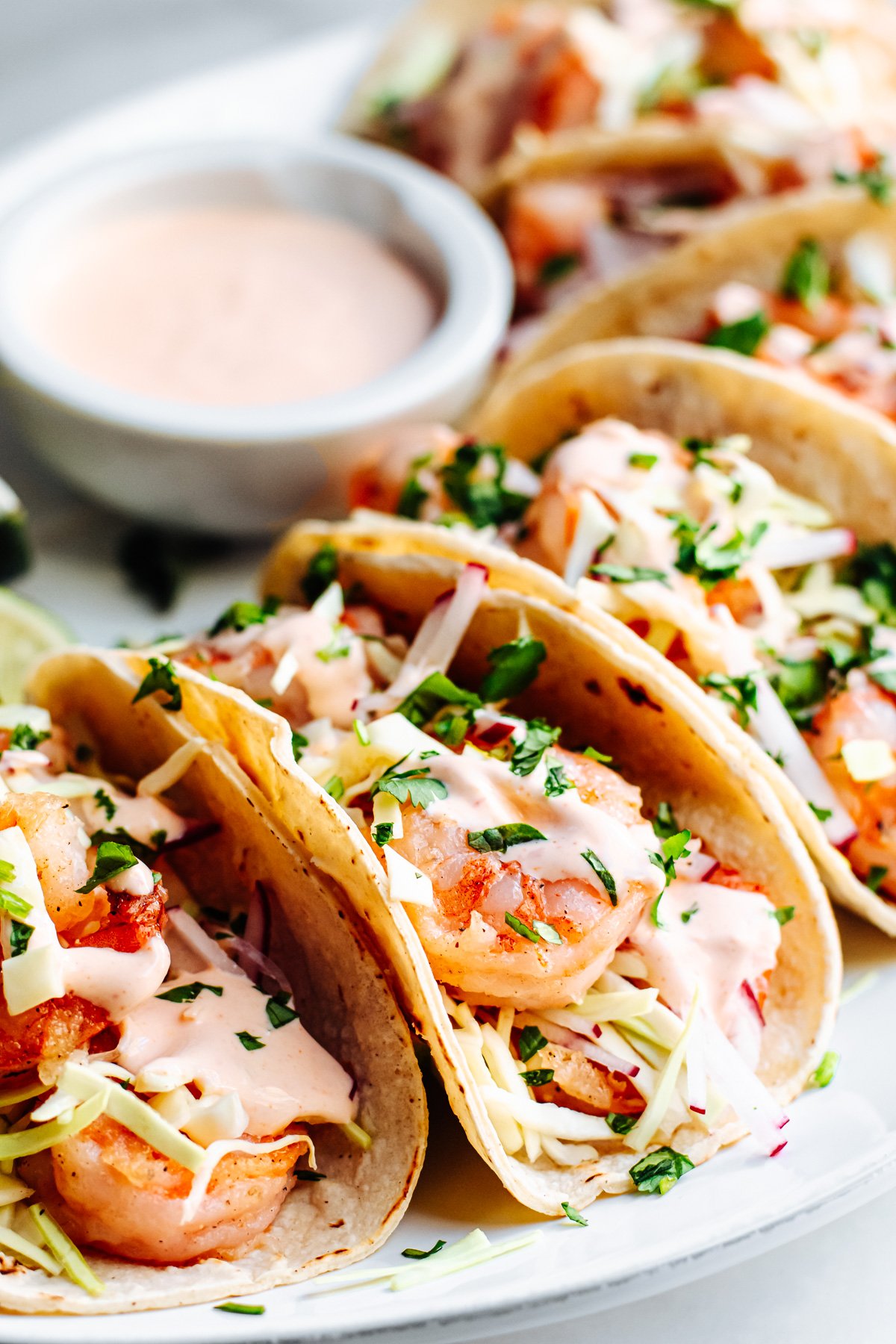 Shrimp Tacos served on a white oval platter with extra sauce on the side.