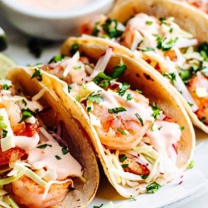 Shrimp Tacos served on a white oval platter with extra sauce on the side.