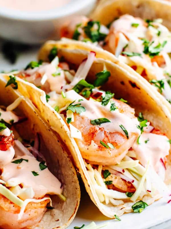 Shrimp Tacos served on a white oval platter with extra sauce on the side.