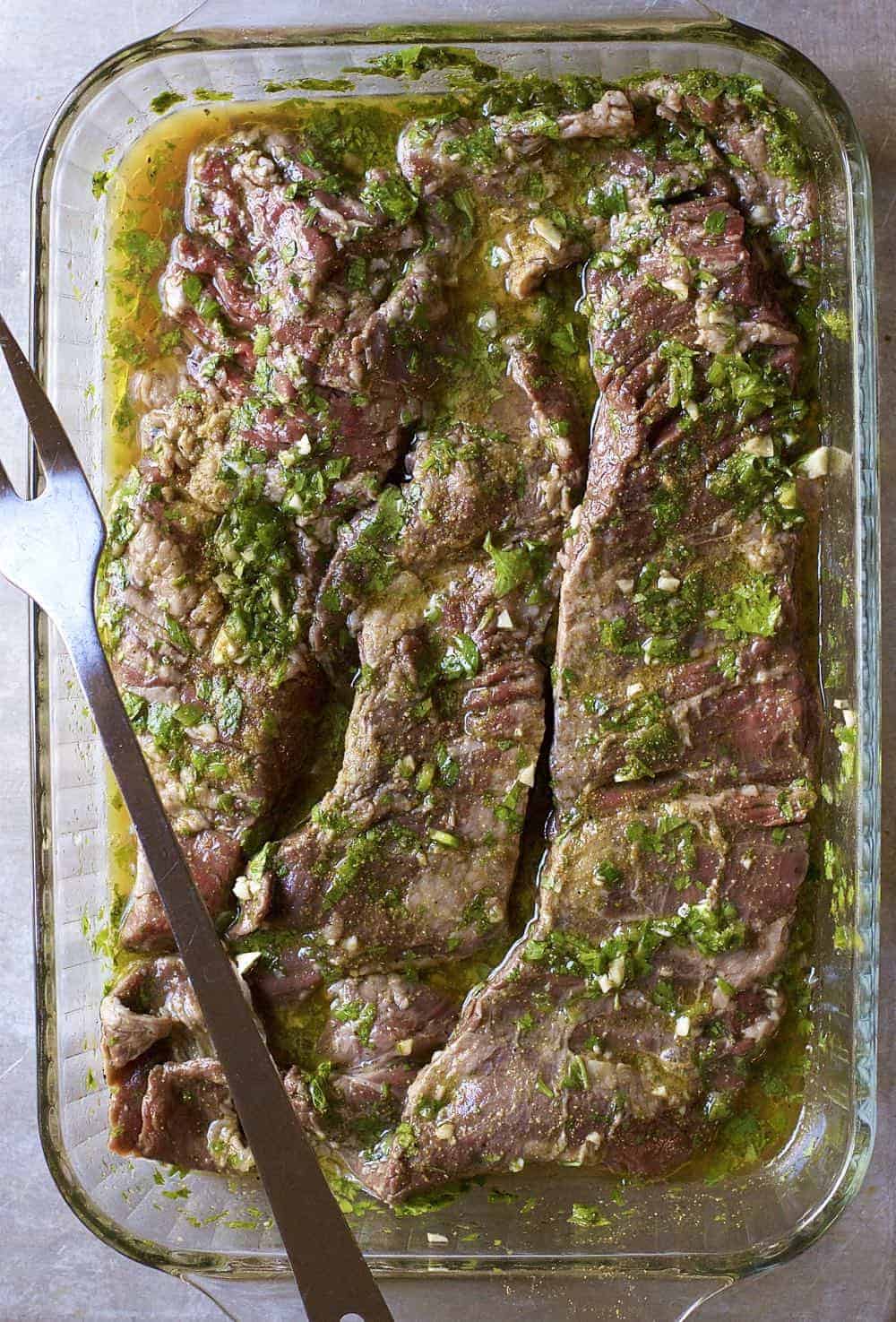 Carne Asada in a glass dish covered in marinade.