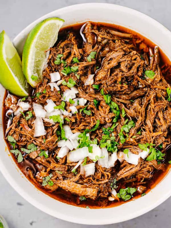 Slow Cooker Birria de Res served in a white bowl with lime wedges.