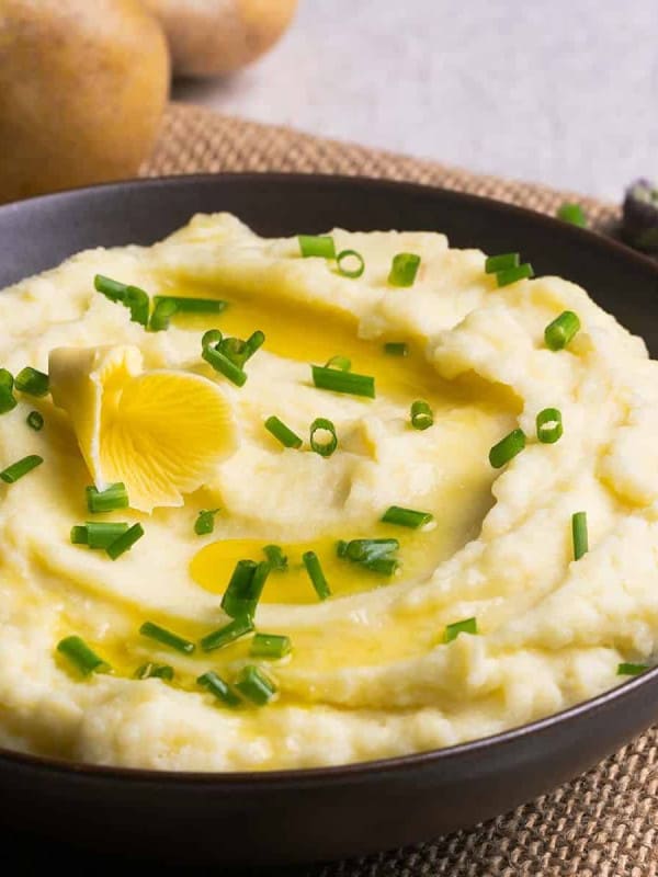 Sour Cream Mashed Potatoes served in a black bowl with butter and photographed at an angle.