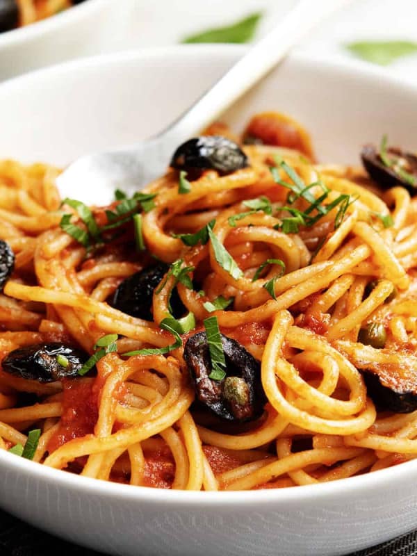 spaghetti alla puttanesca served in a white bowl with a black napkin underneath