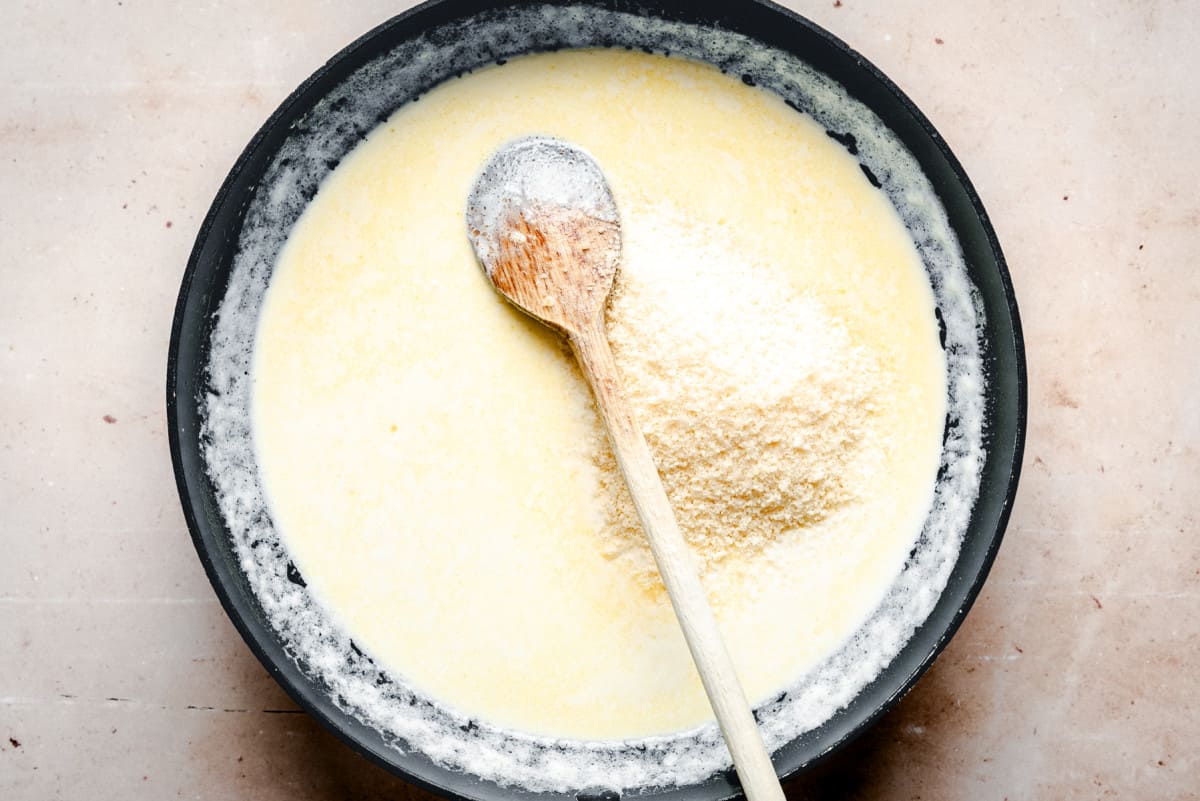 adding grated parmesan to cream sauce in skillet.