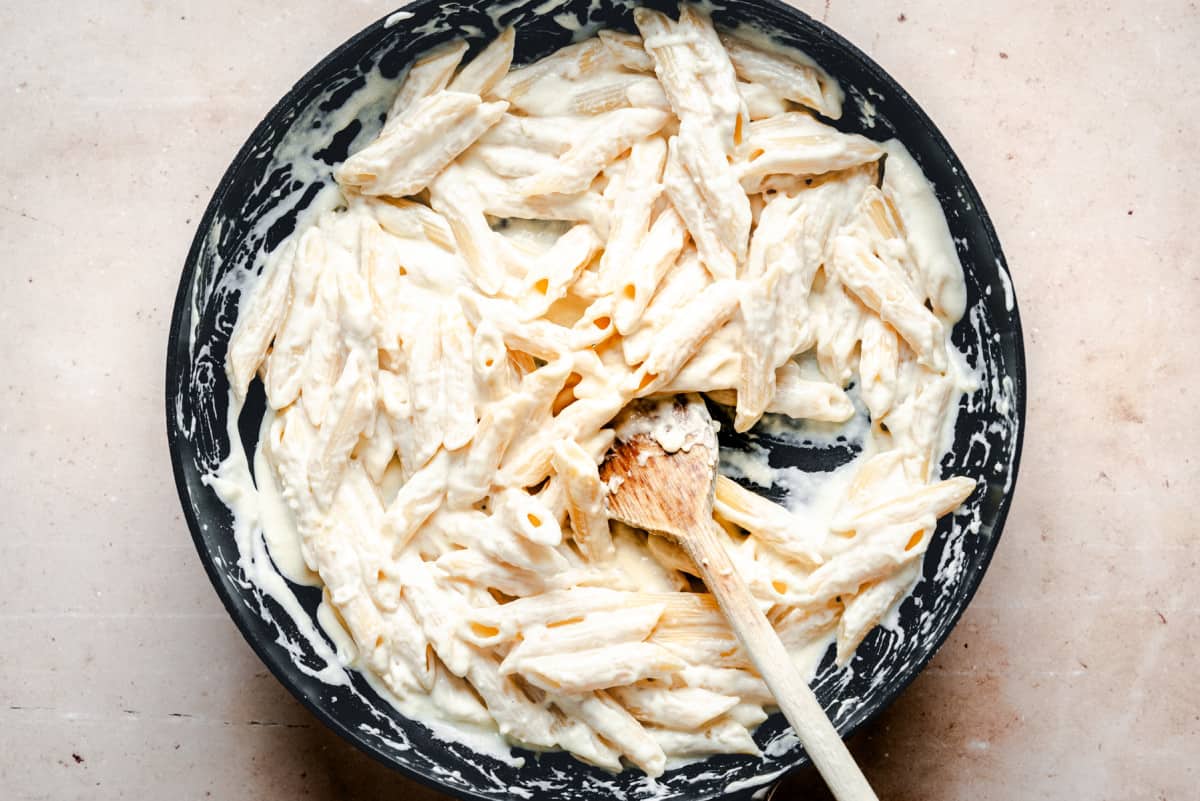 cooked pasta tossed with creamy sauce in skillet.