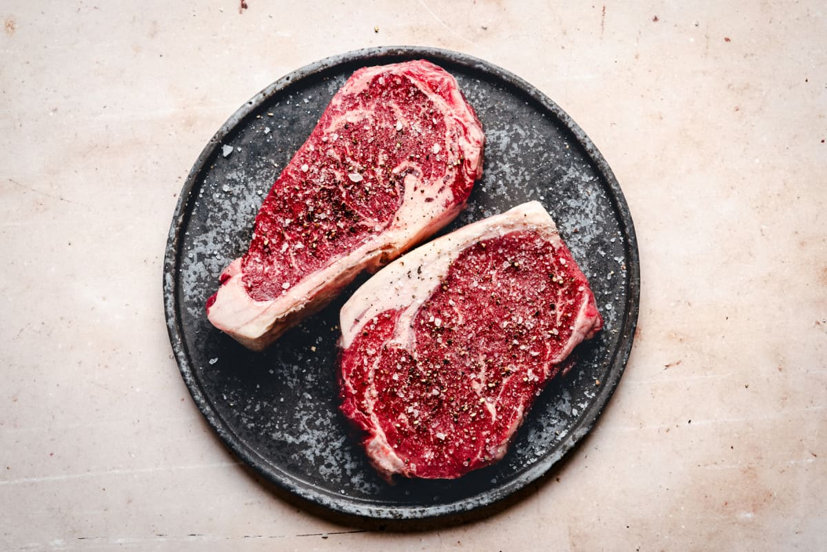 seasoned ribeye steaks on a black plate.