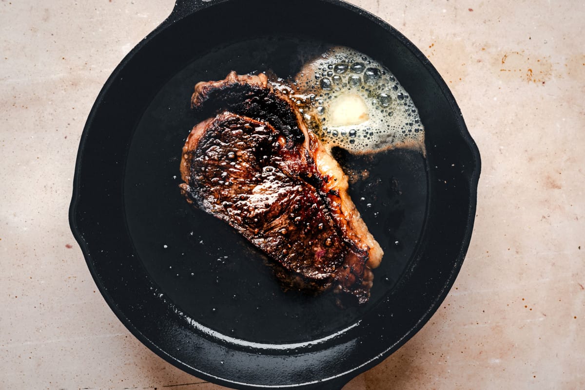 adding butter to seared steak in skillet.