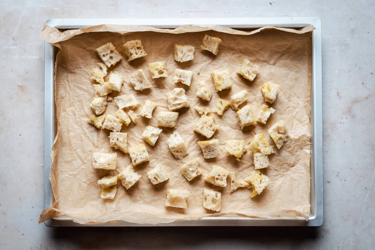 Cubed bread pieces spread on a parchment-lined baking sheet.