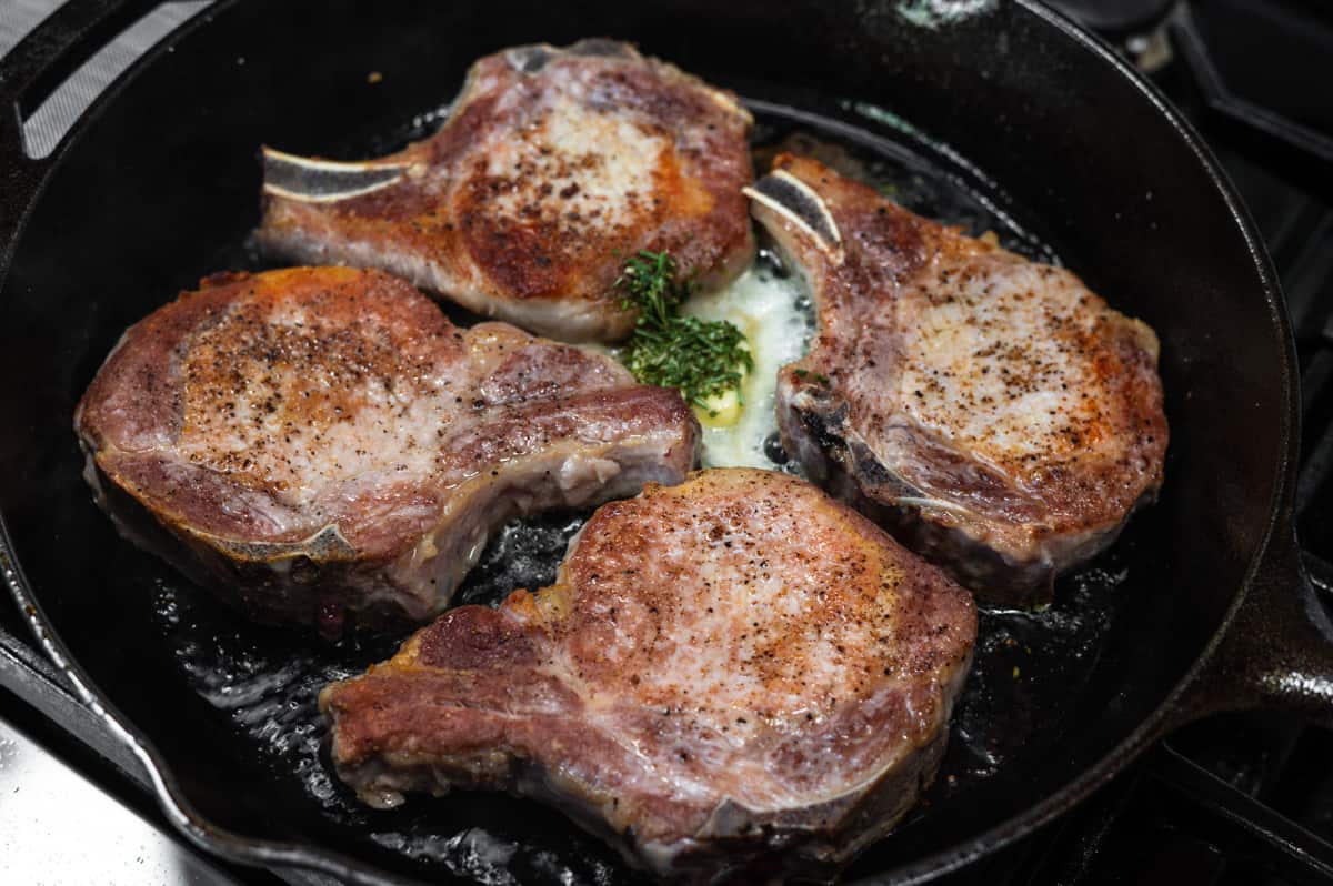 adding butter and rosemary to pork chops in cast iron skillet.