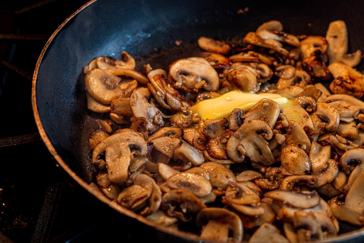 adding butter too cooked mushrooms in skillet.