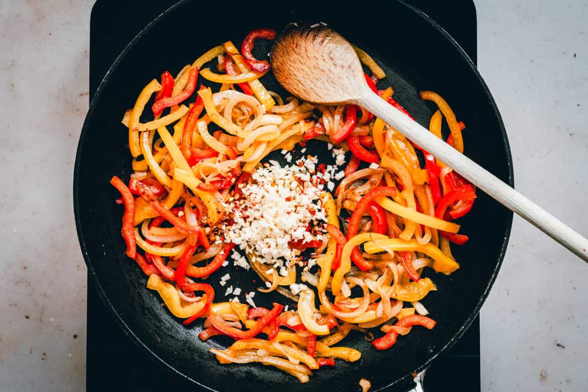 adding garlic to peppers and onions in skillet.