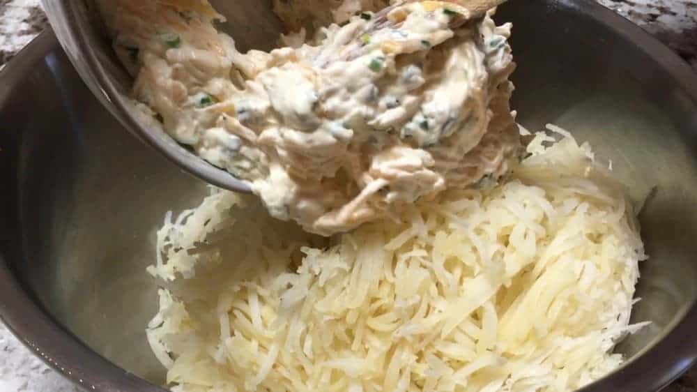 adding sour cream and cheese mixture to shredded potatoes