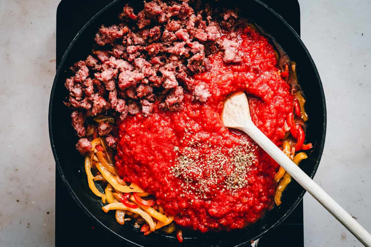 adding tomato sauce seasonings and sausage to cooked pepper mixture.