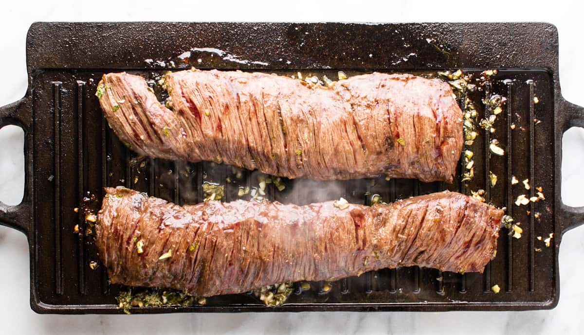 cooked carne asada steak on grill pan with steam rising.