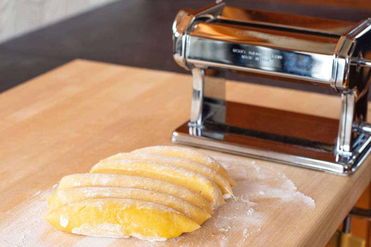 fresh pasta dough cut into portions on floured wooden board