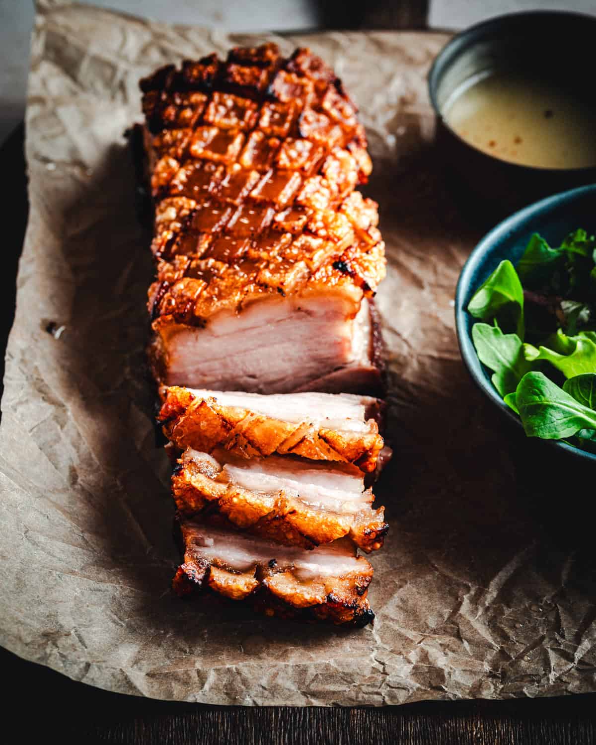 Close up picture of a slab of pork belly with three slices cut from it. Crispy, golden skin and tender meat in the center of the scene.