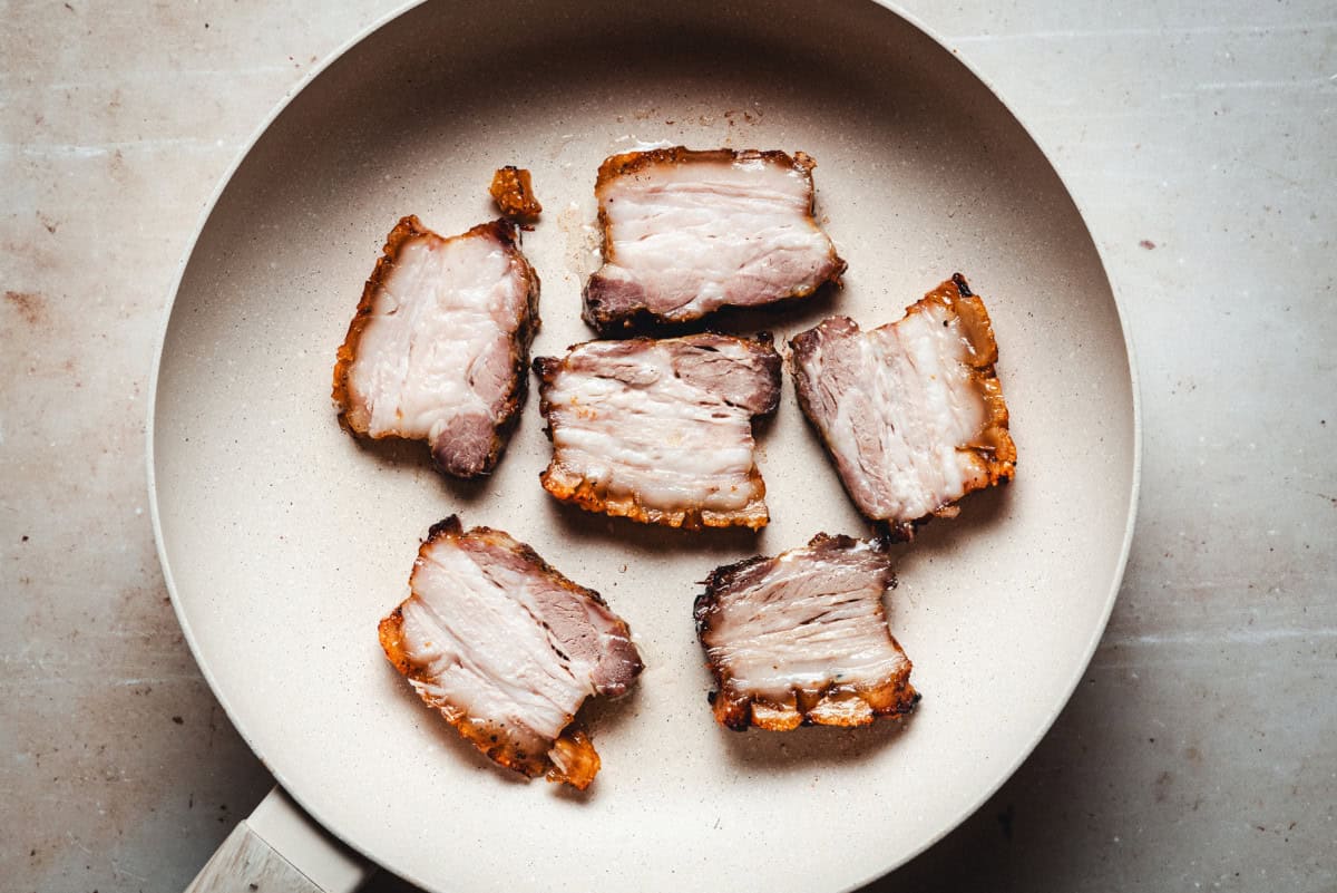 Sliced cooked pork belly in skillet ready to crisp.