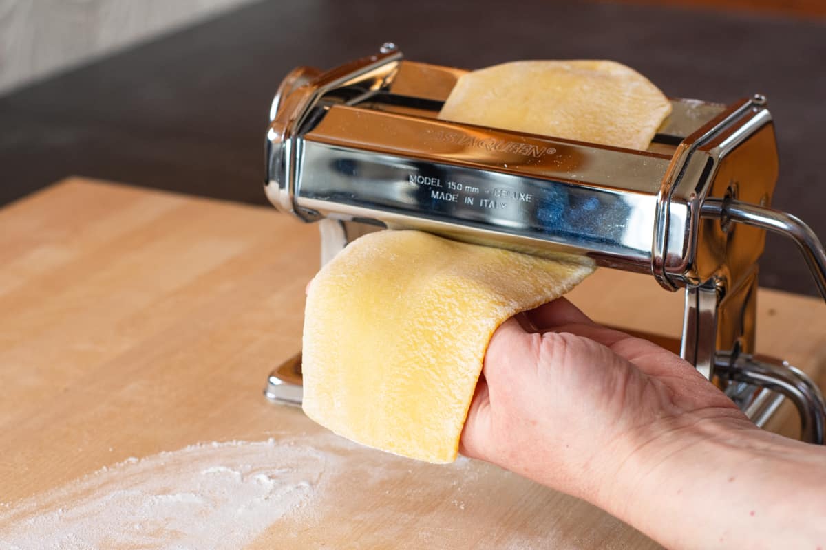 pasta dough passing through manual pasta machine rollers getting thinner