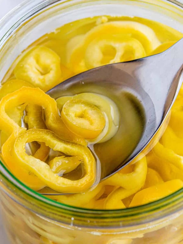 Spooning pickled banana peppers out of a glass jar.