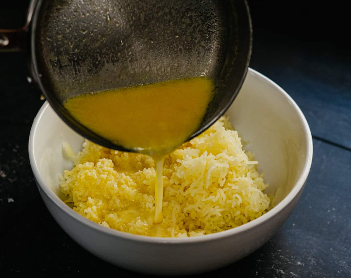 pouring butter garlic and cream mixture over riced potatoes.