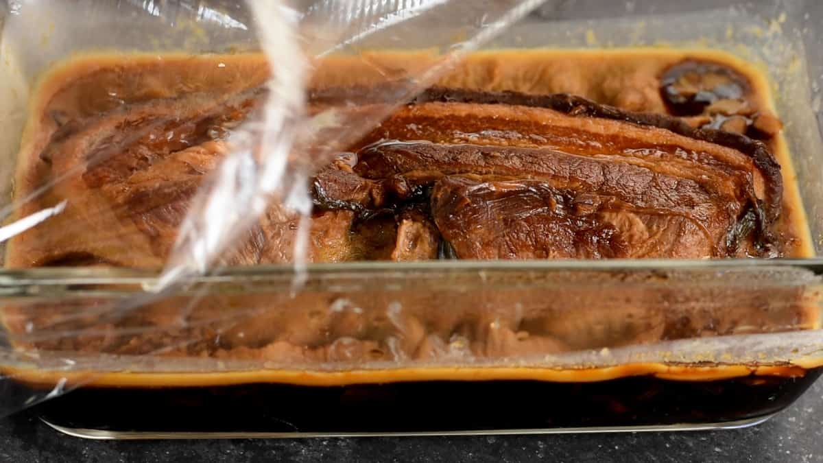 removing plastic wrap after chilling pork belly in braising liquid