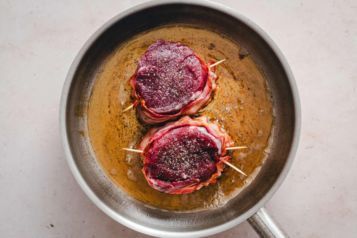 seared bacon wrapped steaks in skillet.