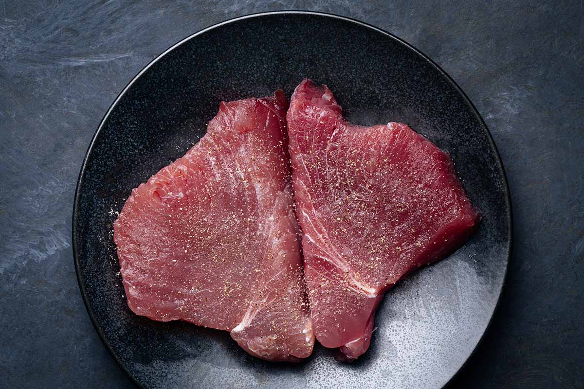 seasoned ahi tuna steaks on a black plate ready to sear.