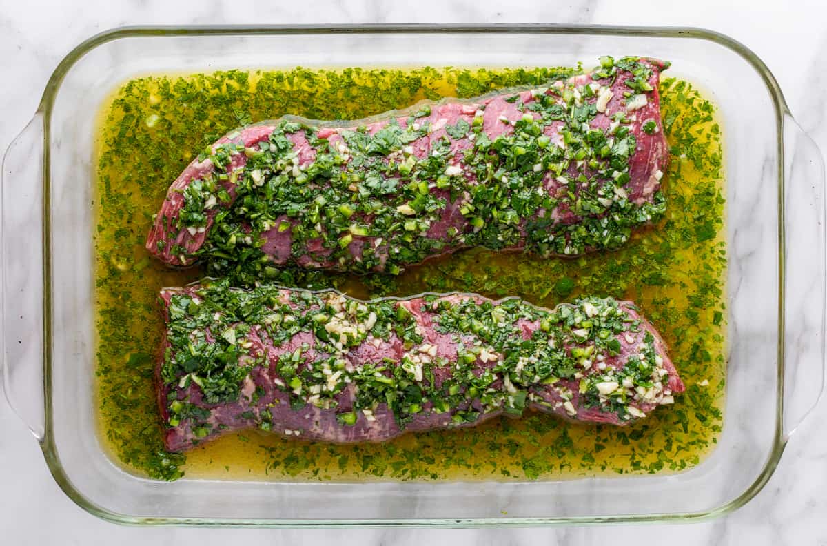 raw skirt steak in carne asada marinade in glass baking dish.