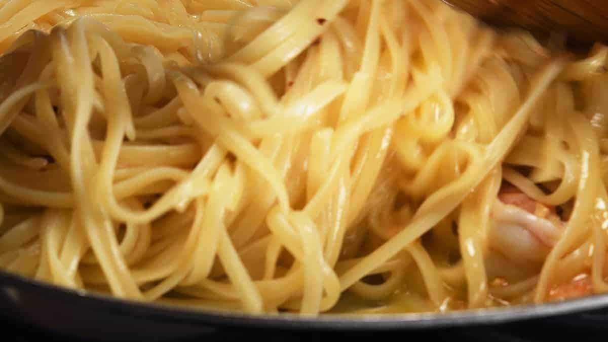 tossing cooked pasta with shrimp and butter olive oil sauce