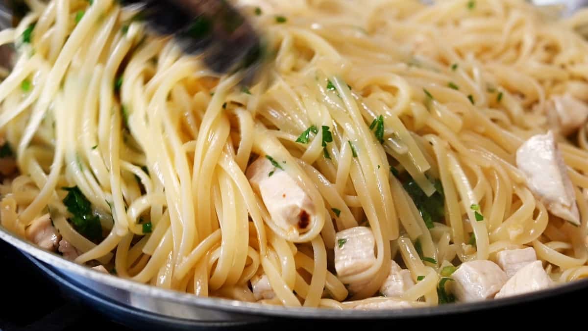 tossing lemon garlic chicken pasta with tongs.